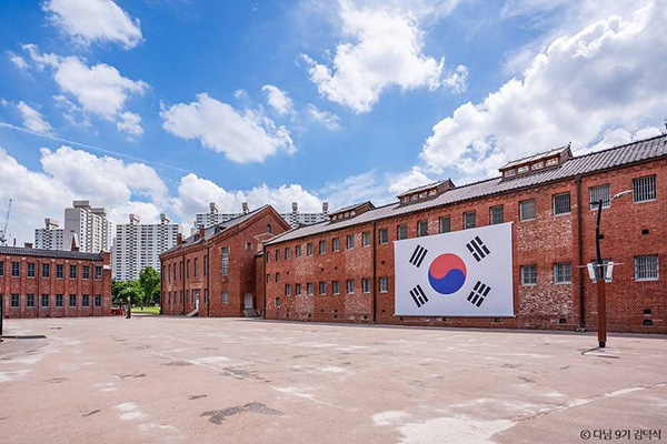 서대문형무소역사관 넓은 앞마당에서 바라본 붉은 벽돌 옥사 외벽에 대형 태극기가 걸려 있는 풍경